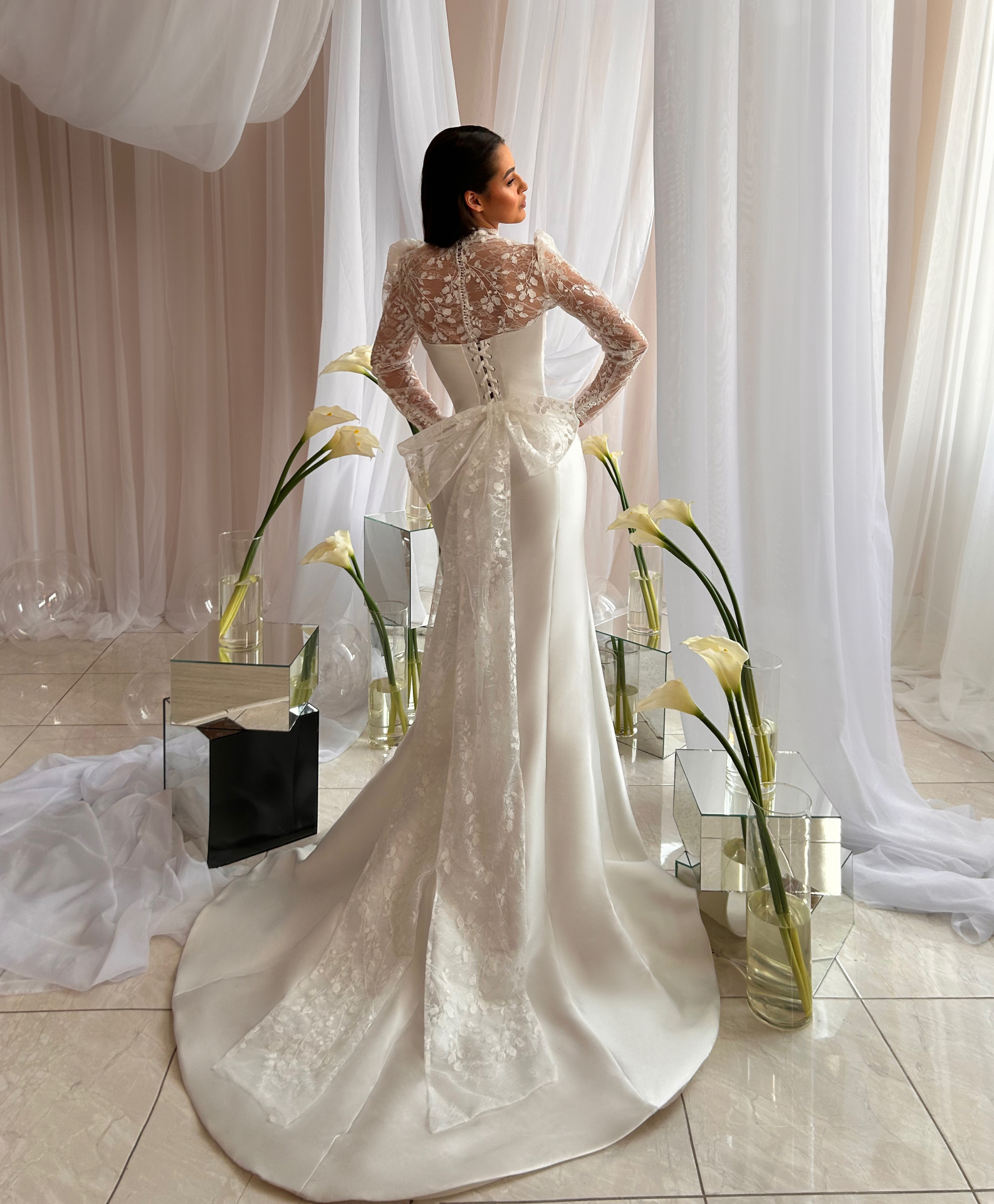 Vlada — back view showing the lace-up corset closure, sheer lace bolero and oversized lace bow over a sweeping satin and lace train